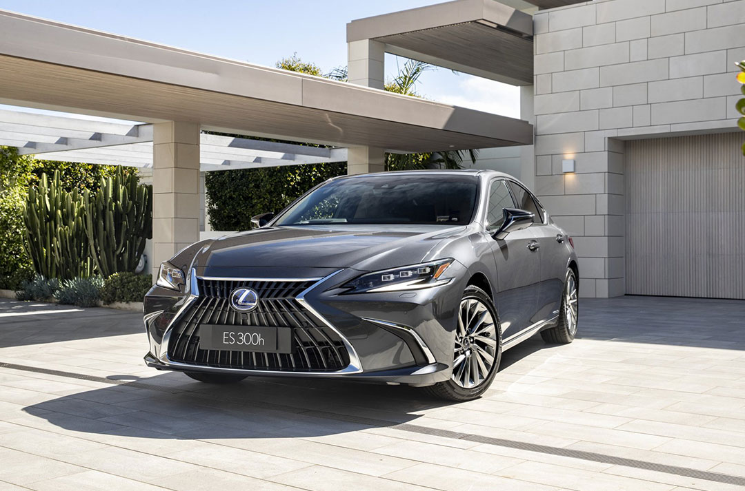 Black Lexus ES 300h parked on a paved driveway in front of building.