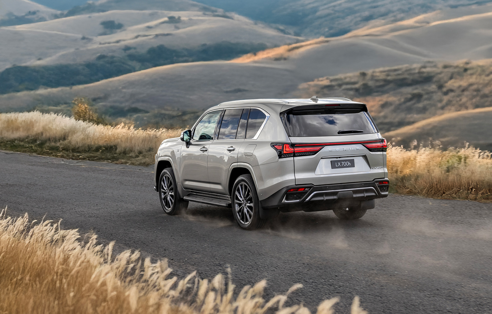 Silver Lexus LX 700h driving on a gravel road through rolling countryside