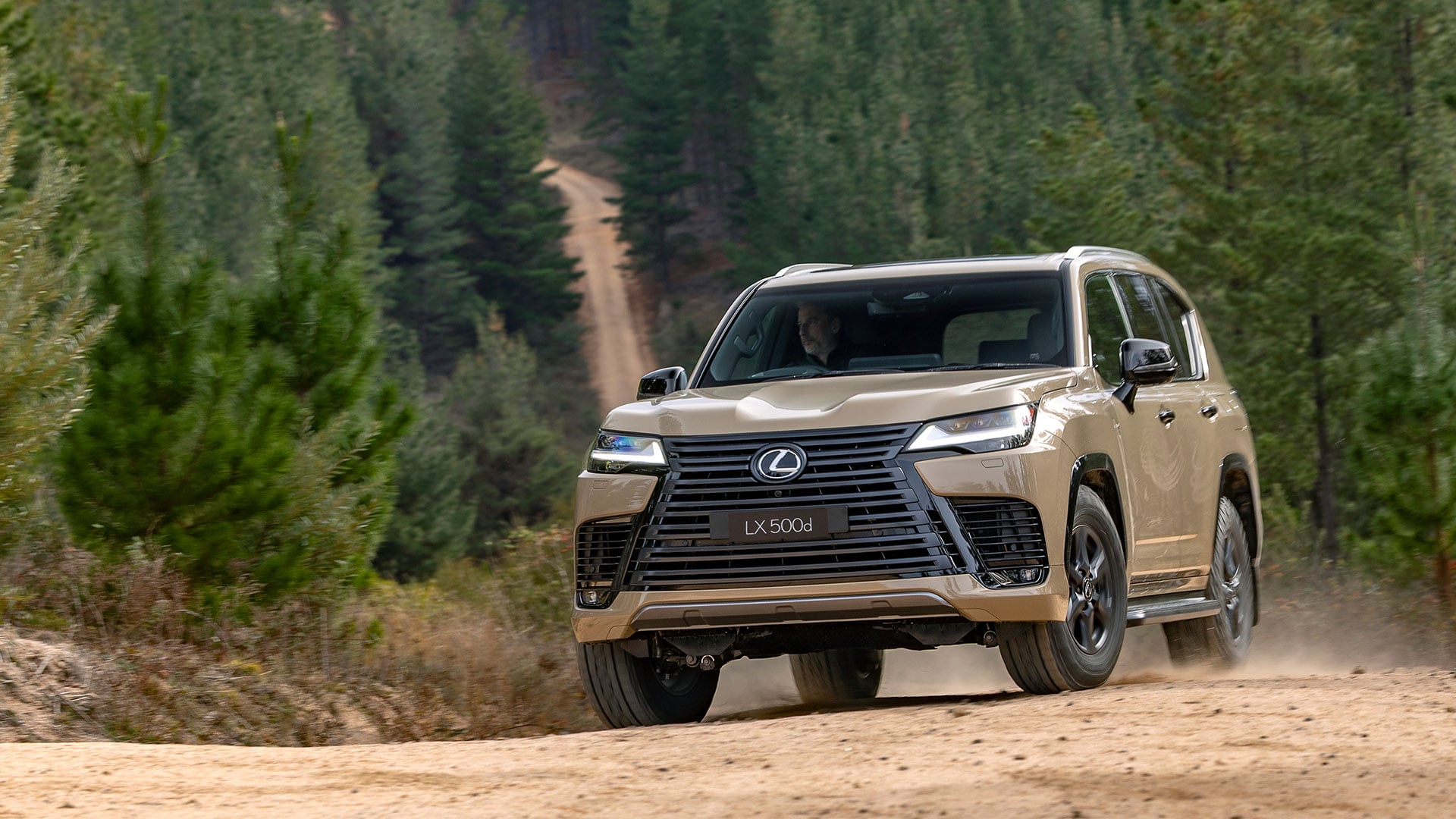 The Lexus LX 500d Overtrail in Earth tone driving on a dirt road surrounded by trees