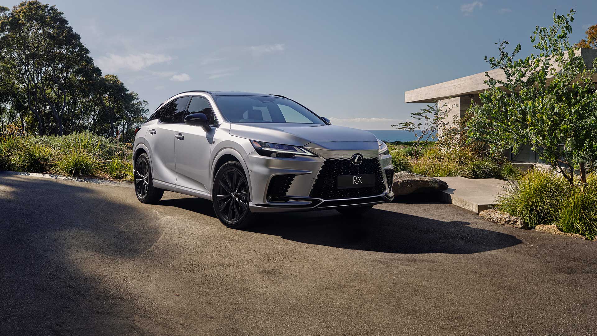 A sliver 2023 Lexus RX parked on a driveway in front of a luxury house.